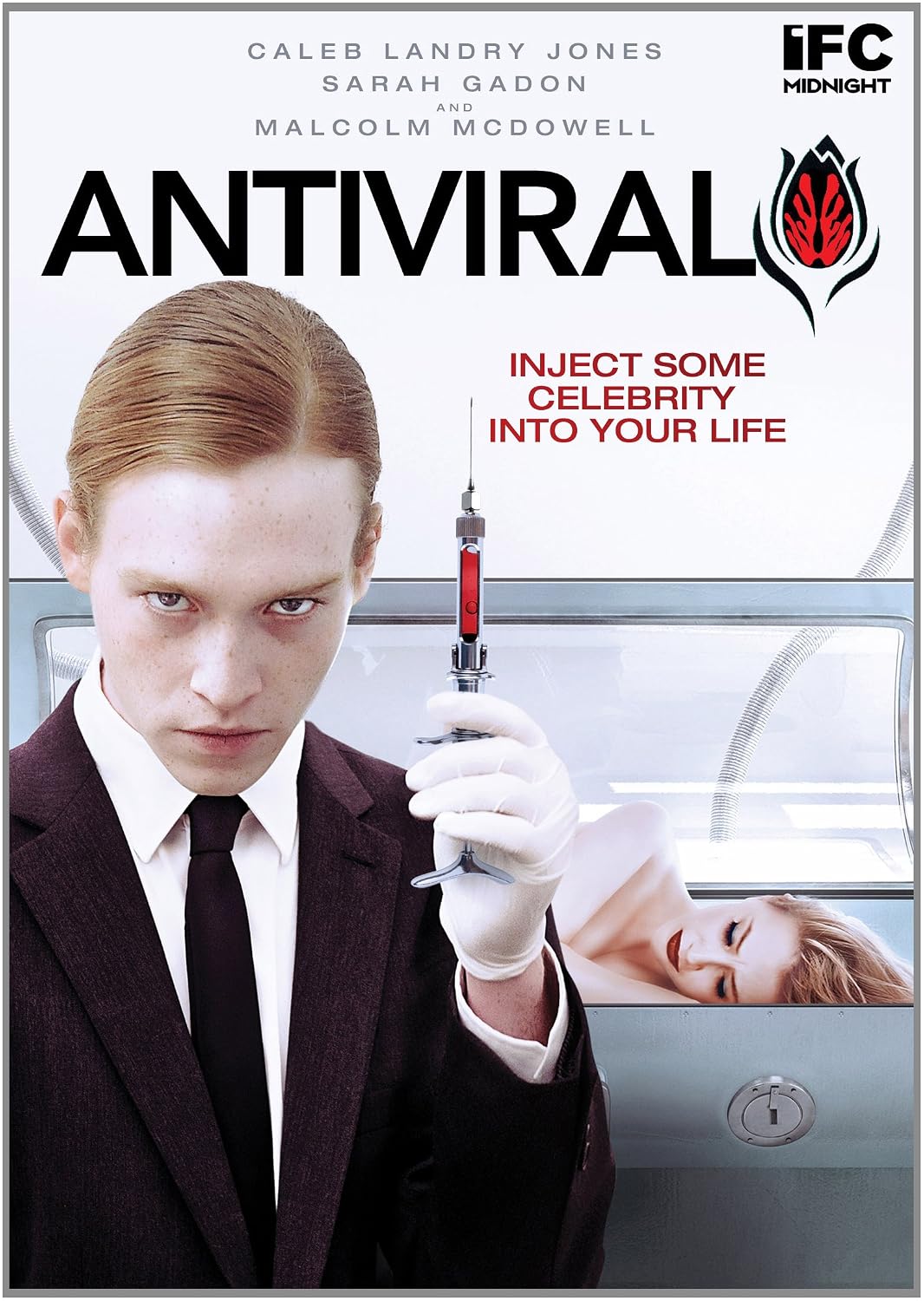 The DVD cover for Antiviral (2012) featuring actors Caleb Landry Jones and Sarah Gadon posing in-character as Syd March and Hannah Geist. Dressed in a black suit and tie, Syd holds a hypodermic syringe filled with blood in his gloved hand, while Hannah lays in a hyperbaric chamber.